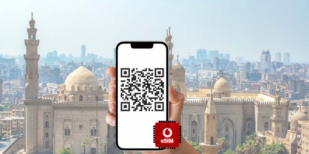 Hand holding a smartphone with a Vodafone eSIM QR code in front of the Pyramids of Giza.